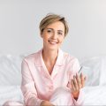 happy-woman-sitting-in-bed-using-cell-phone-2022-01-19-00-11-50-utc-e1659175295343.jpg